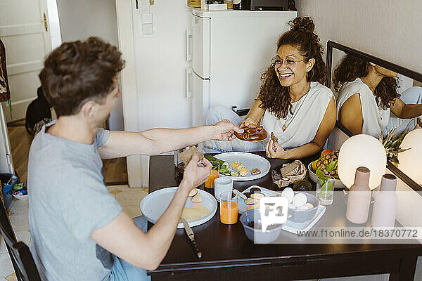 Happy couple sharing food with each other while sitting on dining table at home