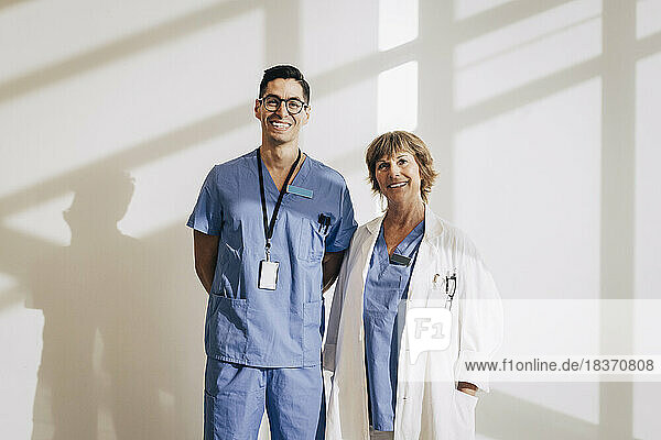 Portrait of happy doctor standing with nurse against wall at hospital
