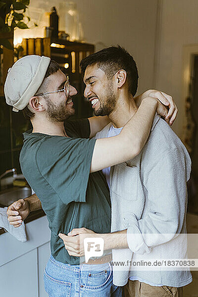 Side view of happy gay couple embracing each other in kitchen at home