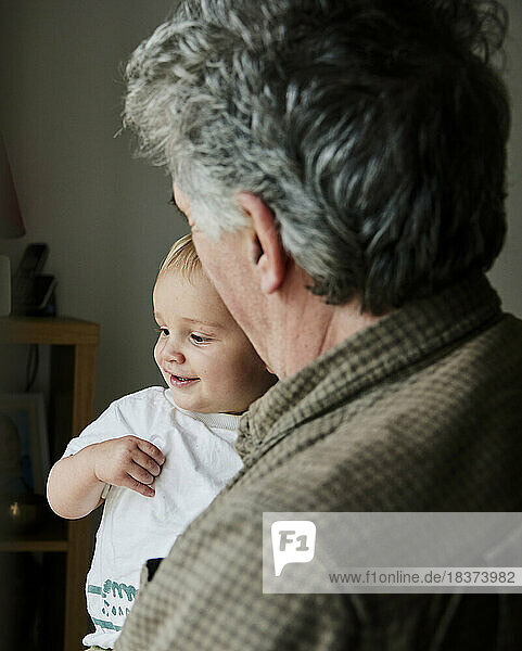 Close up of smiling toddler in arms of grandfather looking out of window