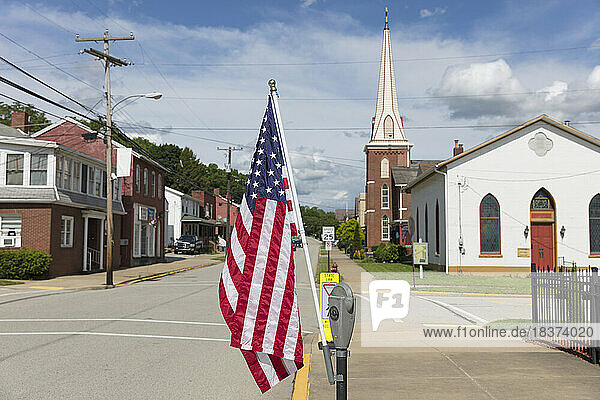 American flag flying on a quiet main street with houses and a church.