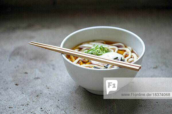 A bowl of noodles  vegetables and broth and a set of chopsticks.