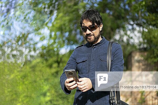Glücklicher junger gutaussehender hispanischer Hipster Mann  der im Park telefoniert