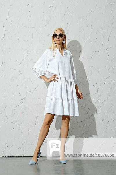 Classy blonde woman in wide white dress posing