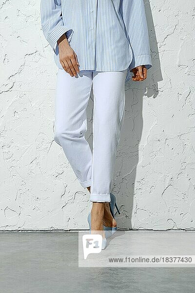Weibliche Beine in weißen Jeans  blauem Hemd und Stilettos