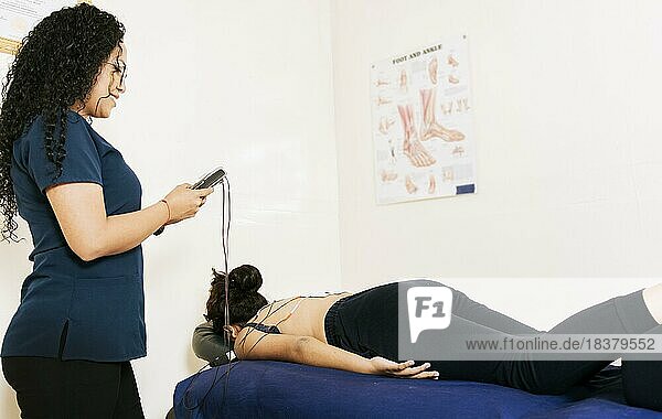 Professionelle Physiotherapeutin bei der Elektrostimulation eines liegenden Patienten. Krankengymnastin bei der Elektrostimulation eines Patienten. Therapie des unteren Rückens mit Elektrodenpads. Elektrodenbehandlung an einem liegenden Patienten  Managua  Nicaragua  Mittelamerika