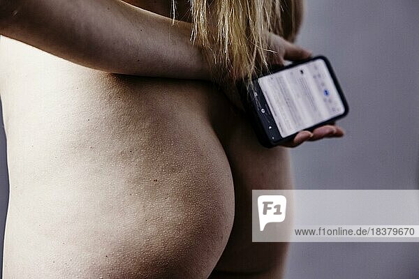 Nackte  junge Frau hält ein Smartphone in der Hand vor ihrem Po  Studioaufnahme  Köln  Nordrhein-Westfalen  Deutschland  Europa