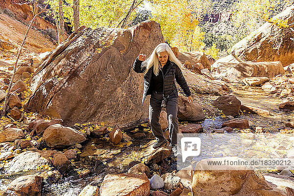 senior blond woman crosses creeks on rocks in Zion National Park Utah