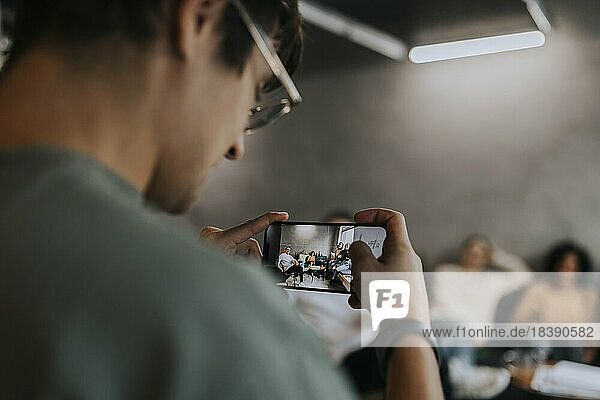 Junger Geschäftsmann fotografiert Kollegen mit dem Smartphone im Kreativbüro