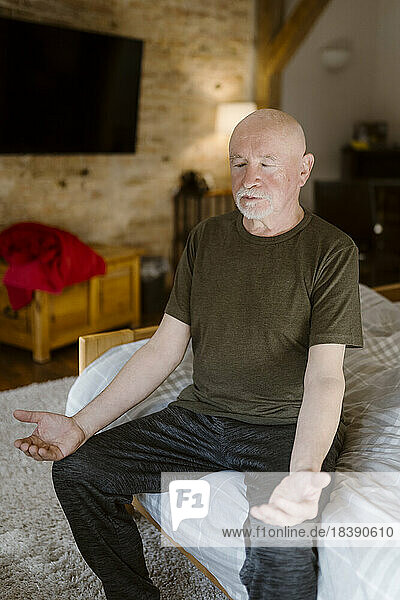 Älterer Mann übt Yoga  während er zu Hause auf dem Bett sitzt