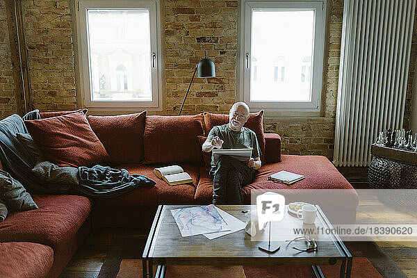 Älterer Mann malt  während er auf dem Sofa im Wohnzimmer zu Hause sitzt