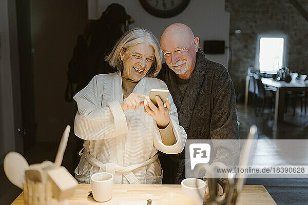 Glückliche ältere Frau teilt Smartphone mit Mann zu Hause