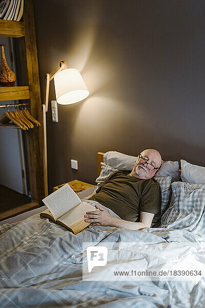 Senior man with book taking nap while lying on bed at home