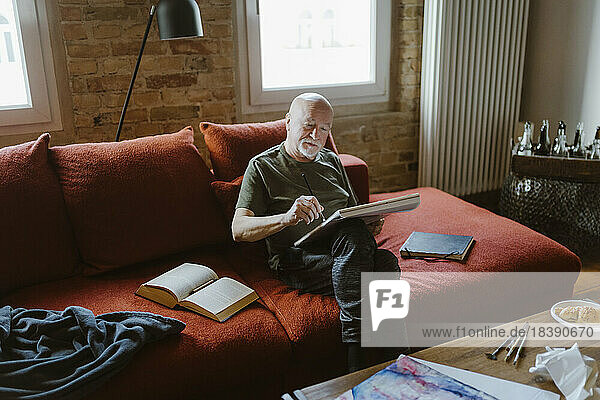 Älterer Mann malt  während er zu Hause auf dem Sofa sitzt