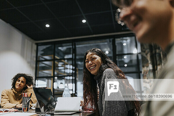 Junge Geschäftsfrau lacht  während sie mit Kollegen während einer Sitzung im Sitzungssaal diskutiert