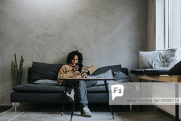 Unternehmerin benutzt ihr Smartphone  während sie auf dem Sofa am Arbeitsplatz sitzt