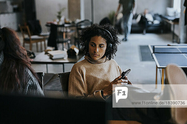 Contemplative businesswoman with smart phone sitting in creative office
