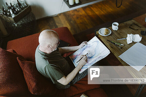 Hohe Winkel Ansicht der älteren Mann malen Gesicht über Papier  während auf dem Sofa zu Hause sitzen
