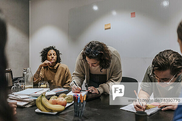 Männliche und weibliche Unternehmer schreiben in Notizblöcke  während sie bei einer Besprechung im Büro eine Strategie diskutieren