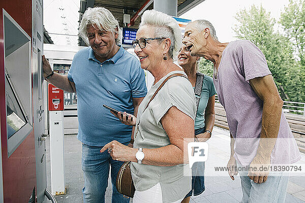 Group of senior friends buying ticket on railway station platform