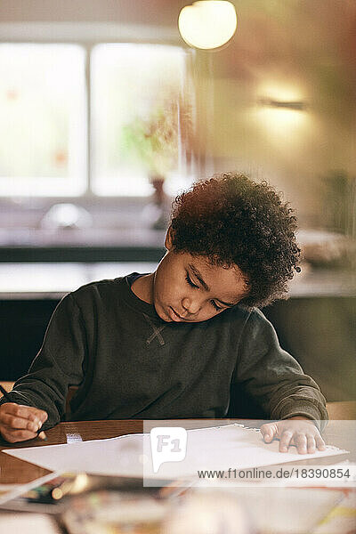 Junge mit lockigem Haar macht Hausaufgaben zu Hause
