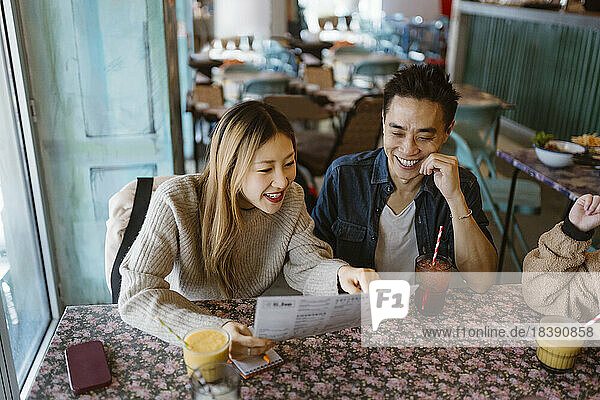 Smiling male and female friends reading menu while sitting together at restaurant