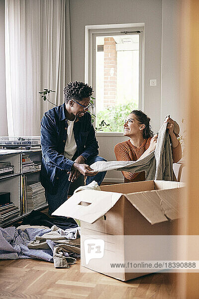 Couple talking to each other sorting out clothes from cardboard box at home