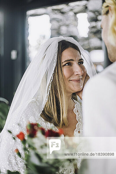 Lächelnde erwachsene Braut im Hochzeitskleid mit Blick auf den Bräutigam