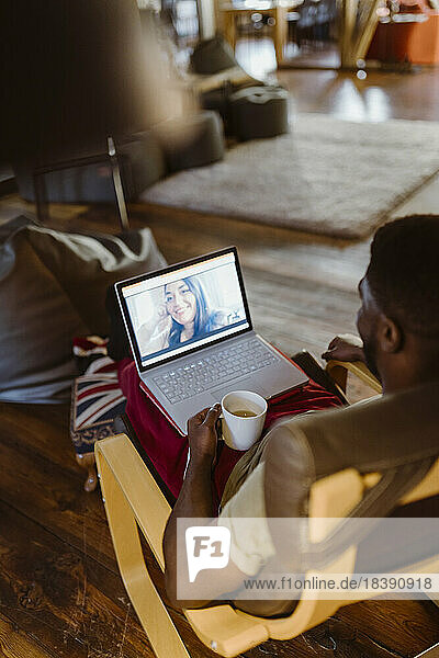 Mann führt Videogespräch mit Frau über Laptop  während er zu Hause auf einem Stuhl sitzt