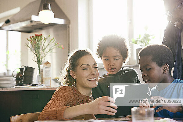 Lächelnde Mutter  die mit ihren Söhnen zu Hause ein digitales Tablet betrachtet