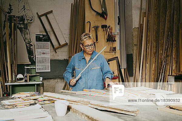 Ältere Handwerkerin misst Holz an einer Werkbank in einer Werkstatt