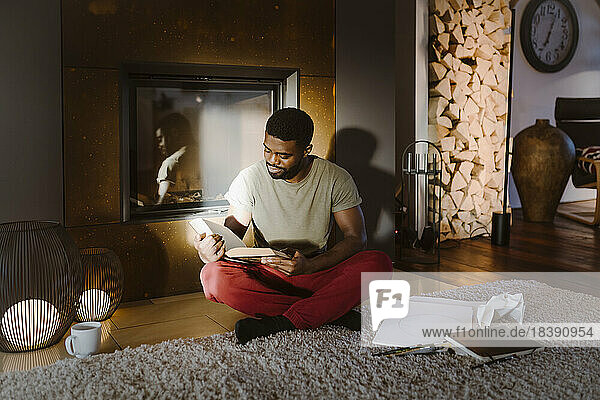 Junger Mann  der im Schneidersitz zu Hause ein Buch liest