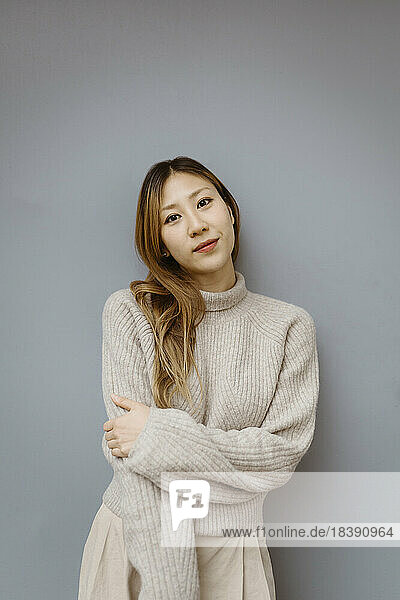 Porträt einer jungen Frau  die einen Pullover trägt und vor einem grauen Hintergrund steht