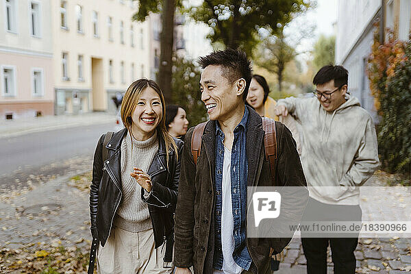 Male and female friends laughing while walking on sidewalk