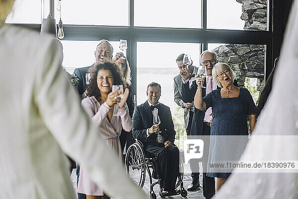 Glückliche multirassische Gäste mit Weingläsern  die dem frisch vermählten Paar bei der Hochzeitszeremonie zujubeln
