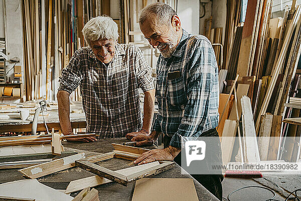 Zufriedene ältere Handwerker  die sich in der Werkstatt Holzrahmen ansehen