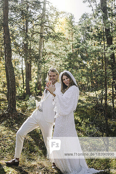 Glückliche Braut und Bräutigam halten die Hände  während sie sich im Wald vergnügen