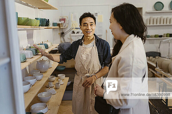 Handwerker  der einer Kundin beim Kauf von Keramik in der Werkstatt hilft