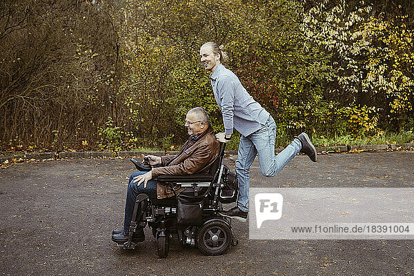 Fröhlicher junger Mann  der auf dem motorisierten Rollstuhl eines älteren Vaters im Ruhestand mit einer Behinderung fährt