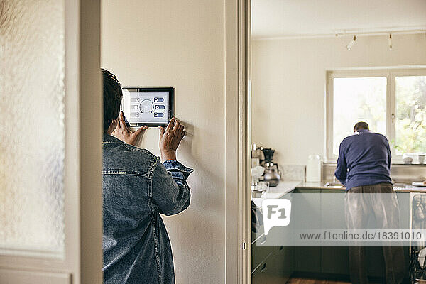 Rückansicht einer Frau  die ein digitales Tablet benutzt  das zu Hause an der Wand befestigt ist