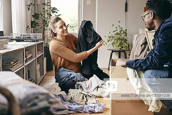 Glückliche Frau zeigt Mann Hemd beim Sortieren von Kleidung zu Hause