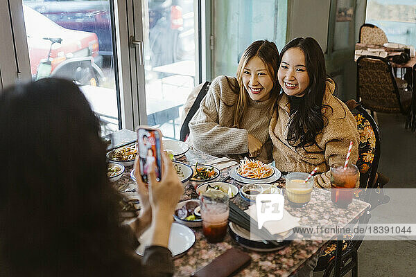 Frau fotografiert Freundinnen  die im Restaurant beim Essen sitzen