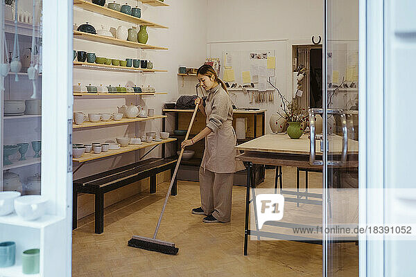 Eine Töpferin reinigt den Boden mit einem Besen  während sie in der Werkstatt steht