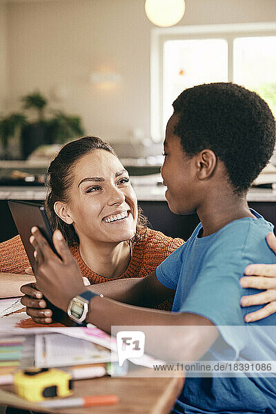 Glückliche Mutter im Gespräch mit ihrem Sohn  der ein digitales Tablet zu Hause hält
