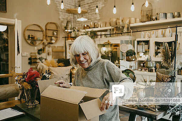 Glückliche ältere Unternehmerin beim Öffnen eines Kartons in einem Geschäft