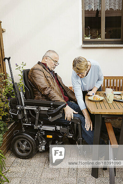 Ältere Frau  die einem behinderten Mann im motorisierten Rollstuhl im Hinterhof hilft