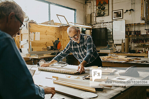 Älterer männlicher Zimmermann prüft Holz auf einer Werkbank in einer Reparaturwerkstatt