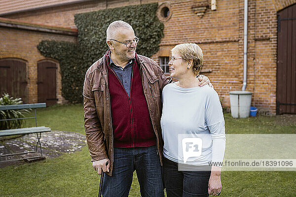 Smiling senior man with arm around woman standing against house at back yard