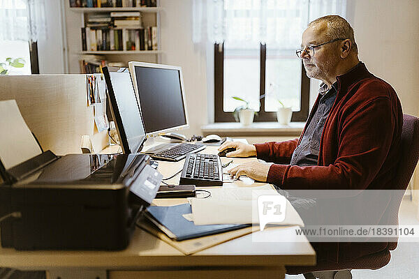 Seitenansicht eines älteren Mannes  der einen Computer am Schreibtisch im Heimbüro benutzt