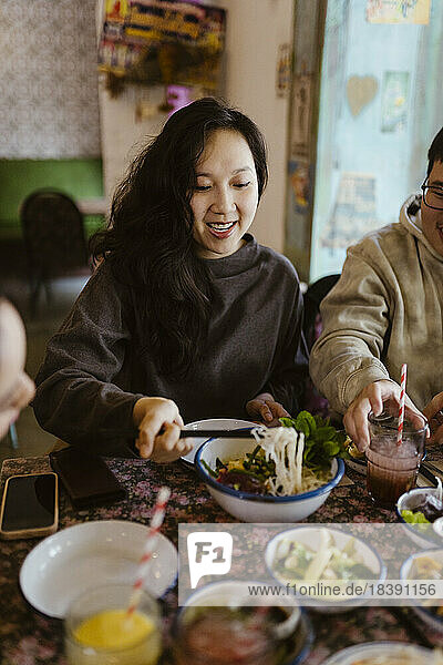 Lächelnde Frau nimmt Essen aus einer Schüssel  während sie im Restaurant sitzt